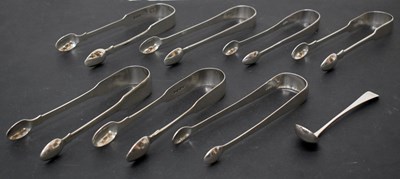 Lot 251 - Seven pairs of George III silver sugar tongs and a silver salt ladle